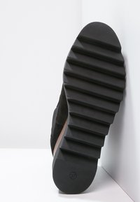 Suela de zapato de ante negro con textura estriada. Presenta una parte inferior de goma negra sólida y un detalle de madera lisa. Talla marcada como 37.