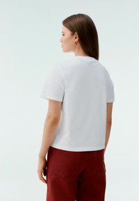 Tricou alb cu mânecă scurtă din bumbac, cu guler rotund și croială lejeră, asortat cu pantaloni roșii cu talie înaltă.