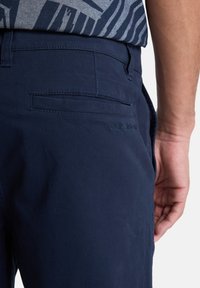 Marineblauwe broek van gladde stof, met een achterzak en subtiele stikseldetails. Casual ontwerp zichtbaar bij de taille.