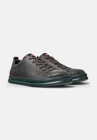Gray leather sneakers with a rounded toe, green rubber sole, and lace-up front. Features small perforations and a red logo tag.