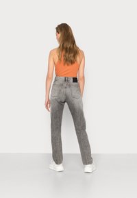 Jeans de ganga cinzentos de perna reta com um acabamento desbotado. Apresenta bolsos traseiros e uma etiqueta preta na cintura. Usados com um top de alças laranja.