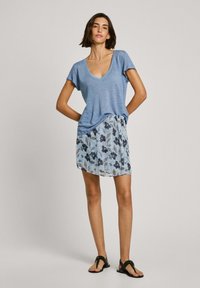 Zils V-veida krekls, kas izgatavots no mīkstas auduma, kombinēts ar gaiši zilu ziedu svārku ar tumšiem rakstiem. Modelis valkā melnus dzīvokļus.