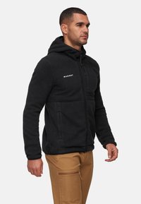 Giacca a zip con cappuccio in fleece nero, superficie testurizzata e logo sul petto. Presenta due tasche laterali e una vestibilità rilassata.