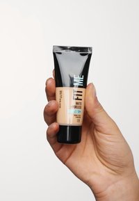 Fond de teint Maybelline Fit Me dans un tube noir et beige, avec une finition mate, une texture lisse et un capuchon noir à vis.