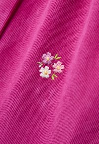 Rosa texturierter Stoff mit einem kleinen gestickten Cluster aus drei Blumen in Hellrosa, Weiß und Lila, umgeben von grünen Blättern.