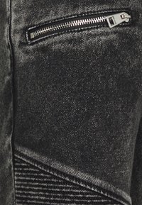 Černá denimová tkanina se vyznačuje strukturovaným povrchem, boční kapsou na zip a akcentovaným prošíváním.