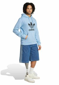 Felpa azzurra con il logo nero di Adidas, abbinata a pantaloncini di jeans e sneakers bianche. Presenta una gamba protesica metallica.