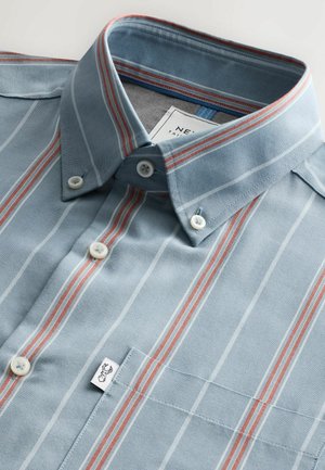 Chemise à rayures bleu clair avec des rayures rouges et blanches, en tissu coton, col pointu, poche poitrine et étiquette avec logo.