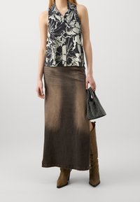 Haut sans manches à fleurs en noir et blanc, assorti d'une longue jupe marron avec un effet ombré. Accessoirisé d'un petit sac noir.