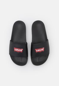 Black slide sandals with a smooth synthetic material, featuring a wide strap and a red Levi's logo on the front. Flat sole, simple design.