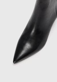 Botte de cheville en cuir noir avec un bout pointu, présentant une texture lisse et un design épuré. Des lignes nettes mettent en valeur son apparence élégante.