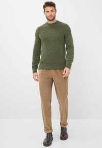 Maglione verde lavorato a maglia con scollatura rotonda, finitura testurizzata, abbinato a pantaloni in velluto a coste marrone chiaro e stivali alla caviglia marrone scuro.