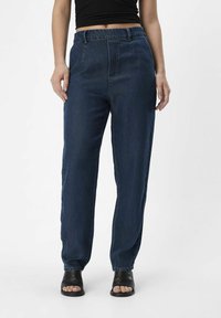 Pantalones de mezclilla azul oscuro con cinturilla elástica, corte recto y bolsillos laterales, combinados con zapatos negros de punta abierta.