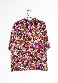 Chemise à manches courtes avec un motif floral dans des tons de noir, orange, rose et blanc ; dotée d'un col et d'un ourlet à volants en bas.