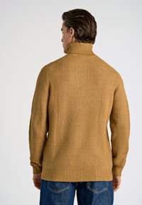 Senapsgul ribbad tröja med hög krage, långa ärmar och texturerad stickning. Har en avslappnad passform och en rak fåll.