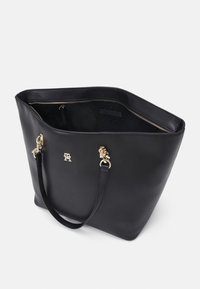 Sac fourre-tout en cuir noir avec ferrures dorées, bretelles d'épaule réglables et poche intérieure zippée, présenté partiellement ouvert sur fond blanc.