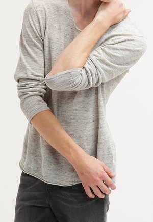Hellgrauer, langärmeliger Strickpullover mit lockerer Passform und strukturierter Oberfläche. Er hat einen V-Ausschnitt und hochgekrempelte Ärmel und wird mit dunklen Hosen kombiniert.