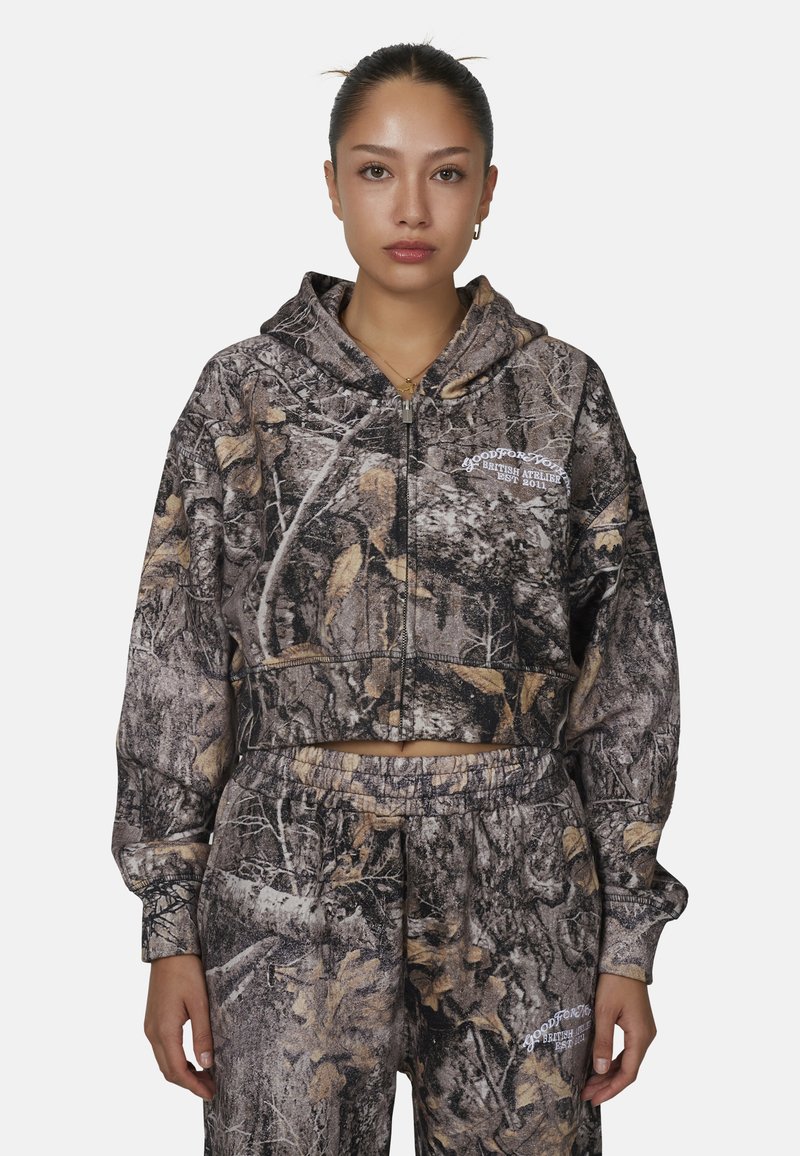 Haut de hoodie zippé coupé en imprimé camouflage avec un mélange de bruns et de verts, doté d'une poche avant et d'un logo graphique sur la poitrine.