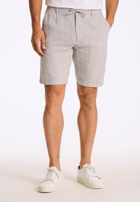 Lichtgrijze shorts met een gestructureerd, gestreept patroon, een koordsluiting in de taille en zijzakken. Gekleed met witte sneakers.