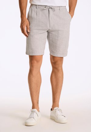 Shorts gris clair avec un motif texturé et rayé, taille élastique avec cordon de serrage, et poches latérales. Associés à des baskets blanches.