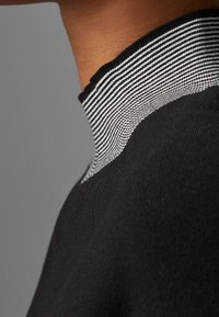 Svart tröja med hög krage och smalt mönster i svart och vitt. Slät yta med en figurnära design, lämplig för lager på lager.