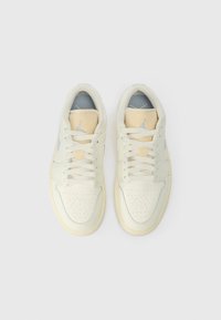 Cremefarbene und hellgelbe Sportschuhe mit einem glatten Lederoberteil, perforierter Zehenbox und weißen Schnürsenkeln. Silberne Akzente und Logodetails.