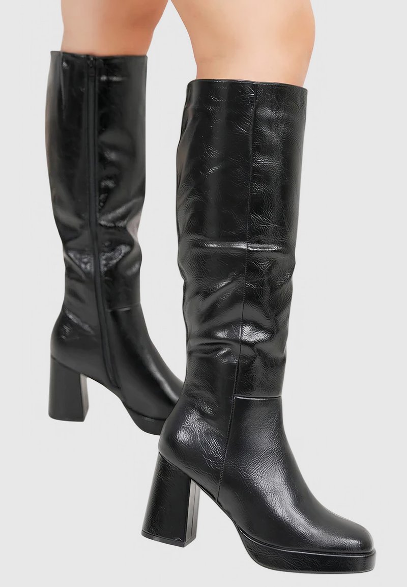 Bottes noires montantes en matériau brillant, avec un talon épais et une texture lisse, dotées d'une fermeture éclair sur le côté pour un enfilage facile.