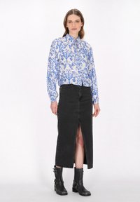 Langärmlige Bluse mit blauem floralen Muster auf weißem Grund, kombiniert mit einem schwarzen Jeansrock mit Schlitz vorne und schwarzen Ankle Boots.