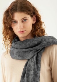 Écharpe en imprimé animal gris en tissu doux, drapée autour du cou. Présente un design texturé avec un léger éclat.