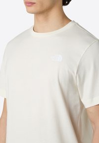 Cream-colored short-sleeve t-shirt made of cotton, featuring a small white logo on the left chest area. Smooth texture, relaxed fit.