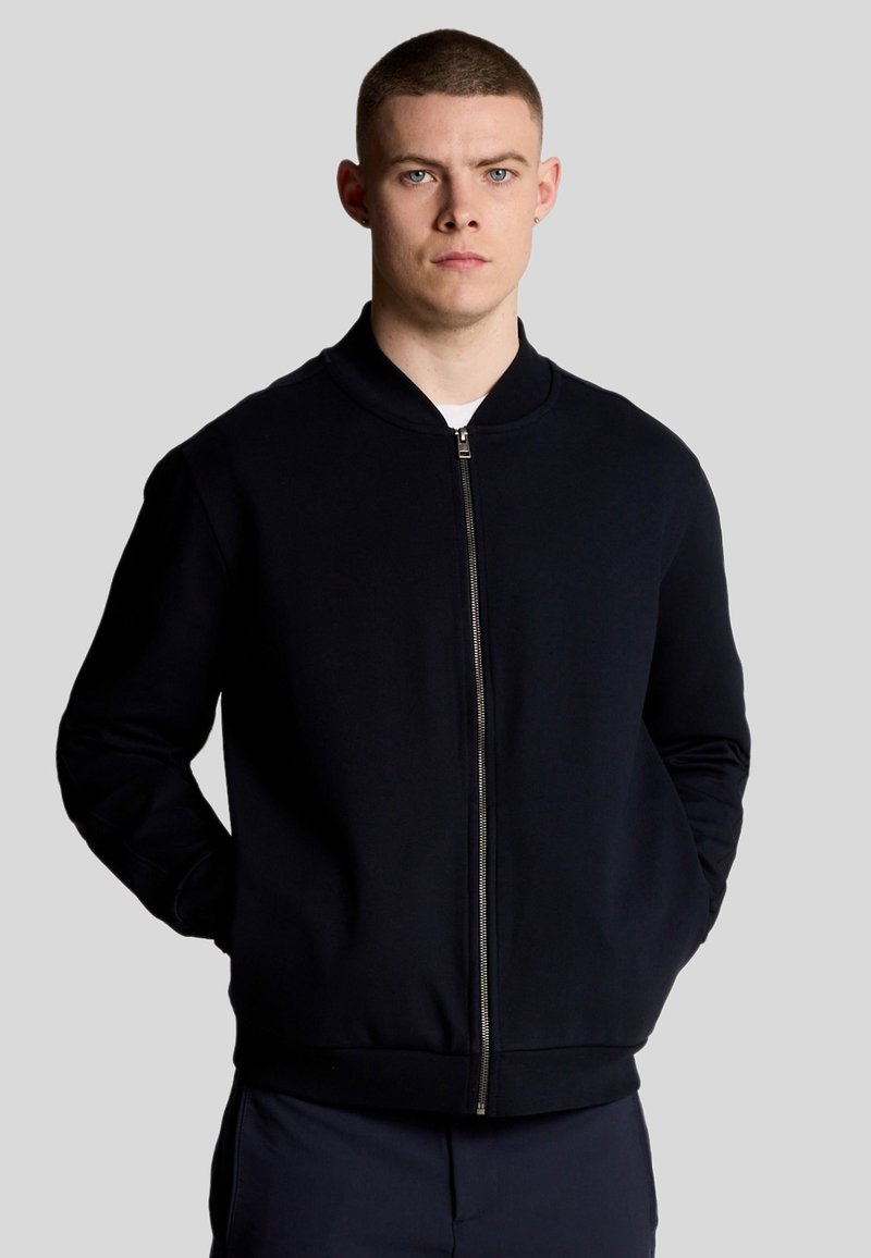 Felpa con zip di colore blu navy, con collo rotondo, polsini e orlo a coste. Tessuto morbido con un design minimalista e senza motivi o loghi visibili.