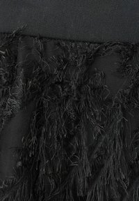 Tissu noir avec des fils effilochés et des détails de fil texturés et emmêlés sur un fond noir tissé lisse.