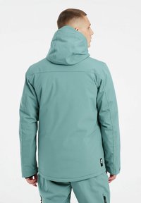 Waterdichte jas in een gedempte teal kleur, met een capuchon, een gladde textuur, elastische manchetten en een label aan de onderzijde links.