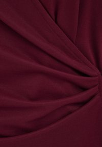 Donkerrood stof verzameld en op één punt vastgenaaid, waardoor stralende plooien en een gestructureerd oppervlak ontstaan.