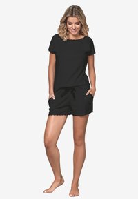 Czarny krótki top z krótkim rękawem i dekoltem o falbaniastym kształcie oraz pasujące szorty z wiązaniem w talii i falbaniastym dołem. Wykonane z miękkiego materiału bawełnianego.