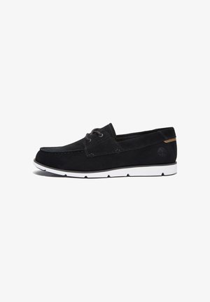 Scarpa da barca in suede nero con suola in gomma bianca, caratterizzata da lacci a contrasto e un piccolo logo sulla parte posteriore. Design classico slip-on.