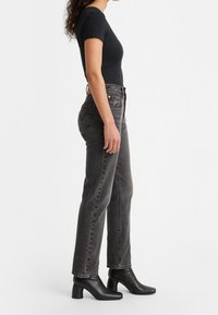 Top negro de canalé de manga corta combinado con jeans gris oscuro de cintura alta y botas de tobillo. Tejido texturizado con corte clásico y ligero estiramiento.