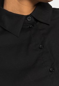 Black shirt featuring a classic collar, five front buttons, and smooth fabric texture. No visible patterns or accents.