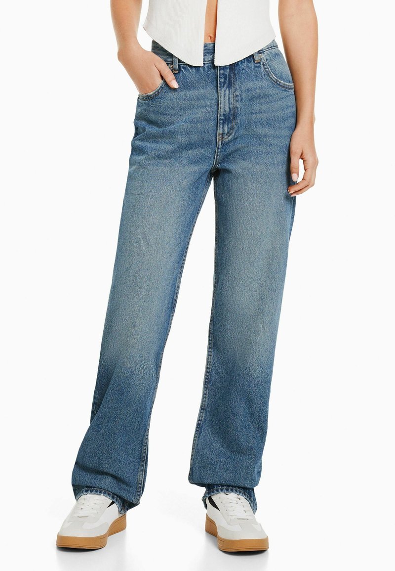 Jeans anchos de mezclilla de color azul claro con cintura alta, bolsillos frontales y un desvanecimiento mínimo. Combinados con tenis blancos para crear contraste.