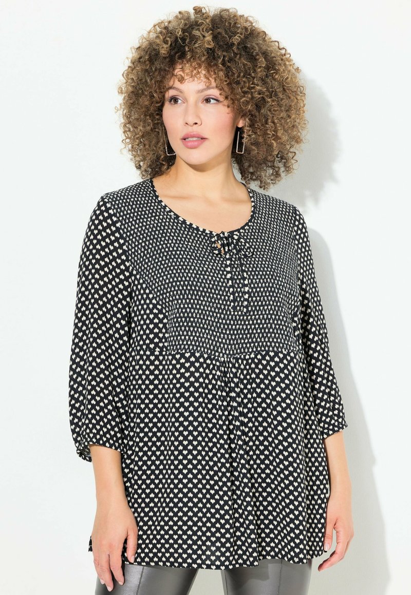 Sort og hvid polka dot top med rund halsudskæring, 3/4 ærmer og en sløjfedetail foran samt en indsamlet design i taljen.