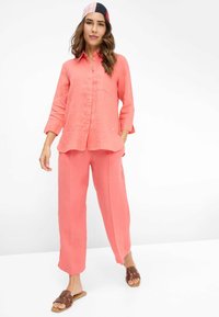 Coral linen shirt with long sleeves, paired with matching wide-leg pants, complemented by brown slides and a patterned headscarf.