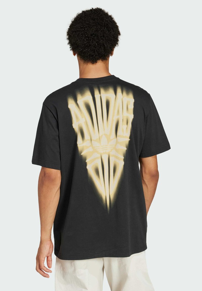 Svart bomullströja med en stor, bleknad gul grafik av "Adidas"-logotypen och emblemet på baksidan, med en lös och avslappnad passform.