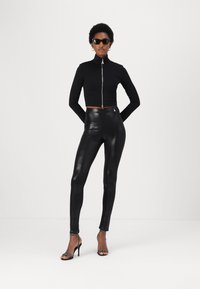 Top cropped nera con zip e maniche lunghe abbinato a leggings neri lucidi e sandali neri con tacco a strappo. Design minimalista, texture liscia.