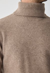 Bézs garbó pulóver, puha kötött anyagból készült. Bordás gallérral és sima, texturált testtel rendelkezik. Egyszerű, klasszikus dizájn.