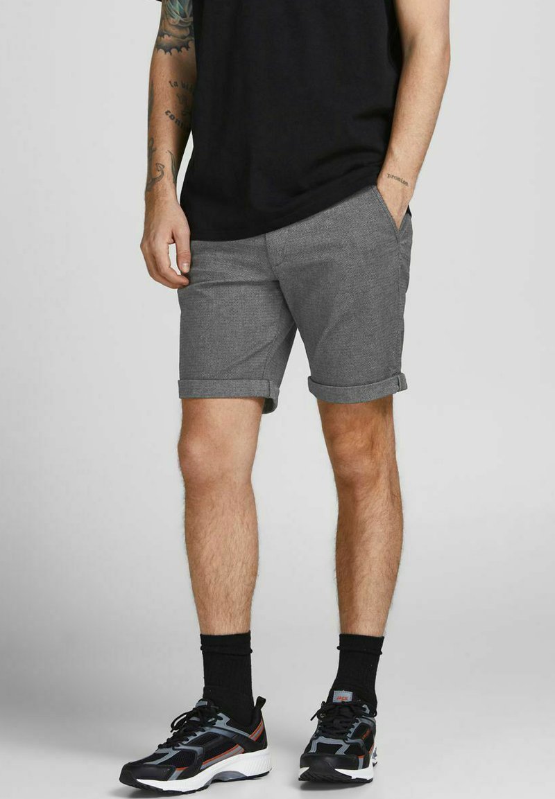 Shorts grisés à motifs avec ourlets roulés, associés à un t-shirt noir et des baskets noires. Présente un design slim fit et un style décontracté.