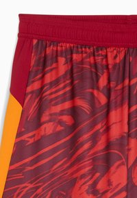 Czerwone i pomarańczowe spodenki sportowe z teksturowanej tkaniny, z wyrazistym abstrakcyjnym wzorem i elastycznym pasem.