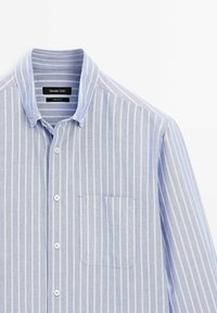 Jasnoniebieska koszula na guziki wykonana z bawełny, z białymi pionowymi paskami, kołnierzykiem oraz kieszenią na piersi po lewej stronie.