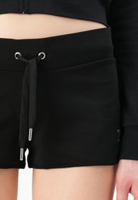 Crne atletske kratke hlače s pojasom na vezanje, srebrnim detaljima i glatkom teksturom. Krojene iznad koljena, s bočnim šavovima za optimalno pristajanje.