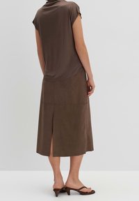 Haut en maille marron avec des manches courtes, associé à une jupe midi en suède marron avec une fente à l'arrière, portée avec des sandales à talons marron.