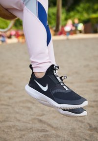 Černá atletická bota Nike s texturovaným svrškem a bílým logem, která má kontrastní bílou podrážku a tkaničky s brandovanými akcenty.